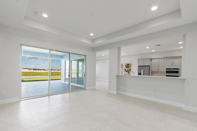 unfurnished living room with recessed lighting, baseboards, and a tray ceiling