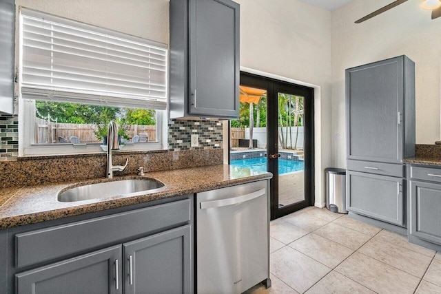 kitchen featuring decorative backsplash, gray cabinets, dishwasher, a sink, and a wealth of natural light