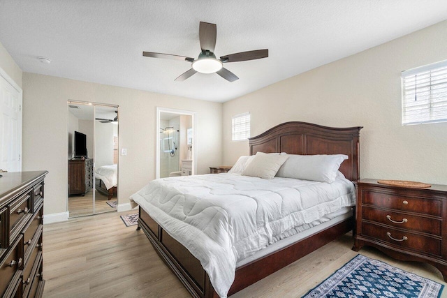 bedroom featuring light wood-style floors, baseboards, ceiling fan, and ensuite bath