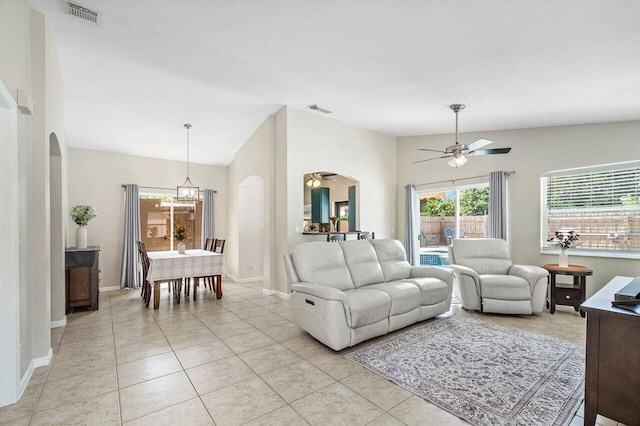 living room with visible vents, lofted ceiling, light tile patterned flooring, arched walkways, and ceiling fan with notable chandelier
