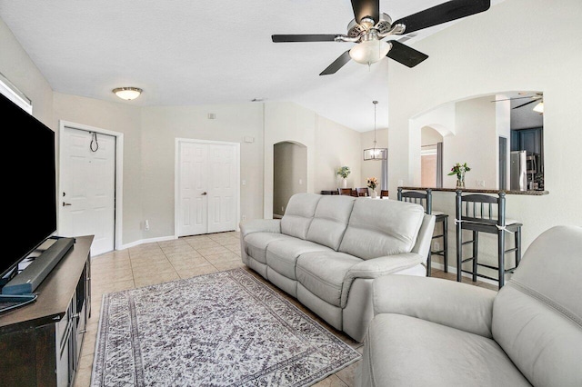 living area featuring ceiling fan, arched walkways, light tile patterned floors, baseboards, and lofted ceiling