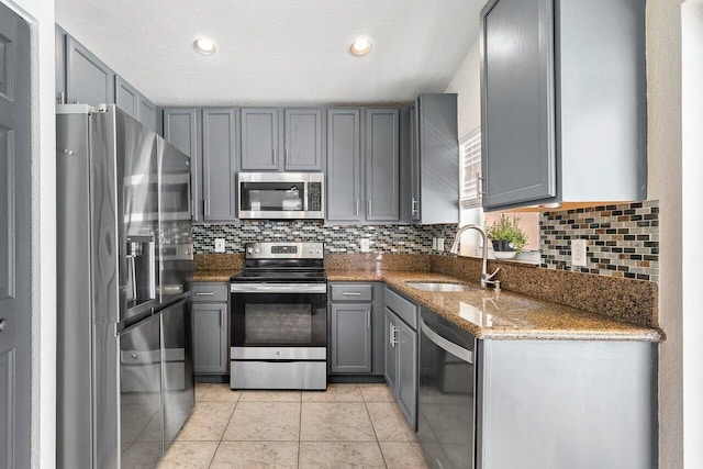 kitchen featuring appliances with stainless steel finishes, a sink, stone countertops, tasteful backsplash, and gray cabinetry