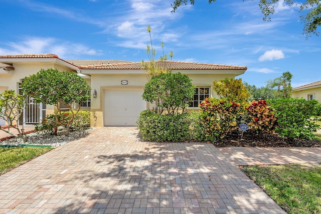 mediterranean / spanish-style home with a garage, stucco siding, decorative driveway, and a tiled roof