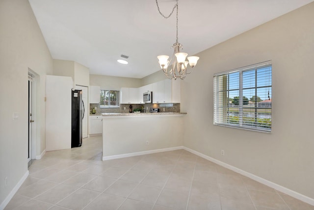 kitchen featuring a notable chandelier, freestanding refrigerator, white cabinetry, stainless steel microwave, and decorative backsplash