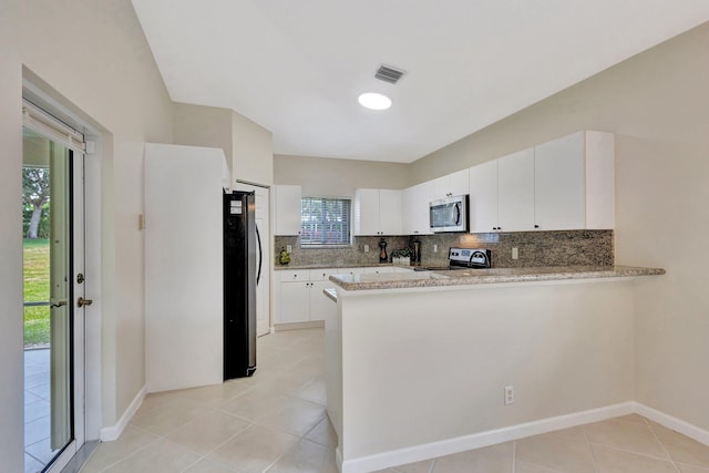 kitchen featuring decorative backsplash, appliances with stainless steel finishes, light tile patterned floors, white cabinets, and a peninsula