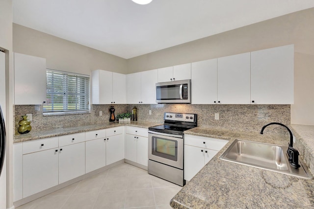 kitchen with decorative backsplash, a sink, light tile patterned floors, stainless steel appliances, and white cabinetry