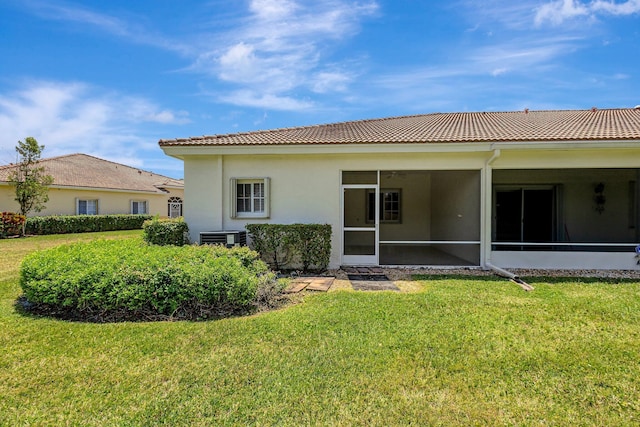 rear view of property with a yard, a tiled roof, and a sunroom