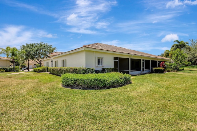 rear view of property with a tiled roof, a lawn, and stucco siding