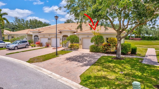 mediterranean / spanish home with a tiled roof, a front yard, decorative driveway, an attached garage, and stucco siding