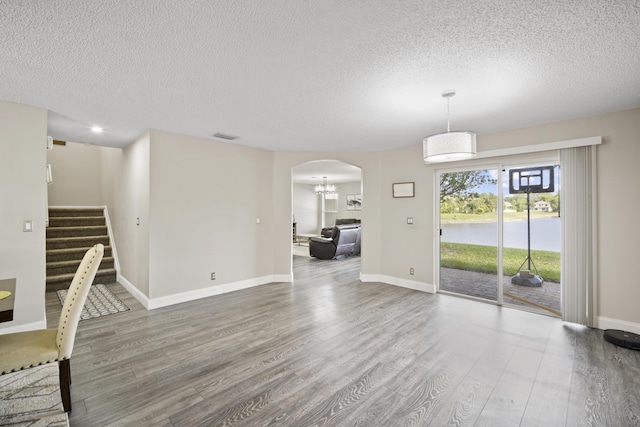 unfurnished dining area with stairs, arched walkways, a textured ceiling, and wood finished floors