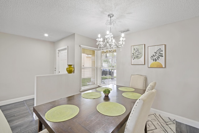 dining room featuring a textured ceiling, visible vents, wood finished floors, baseboards, and a chandelier