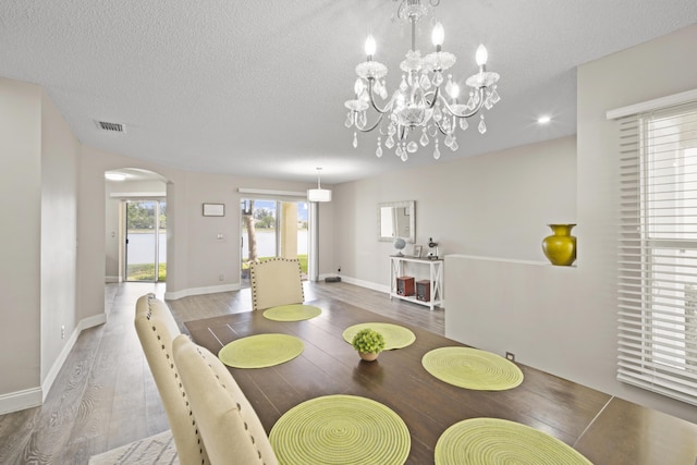 dining space featuring visible vents, arched walkways, a textured ceiling, and wood finished floors