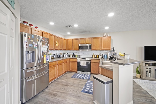 kitchen with visible vents, a peninsula, a sink, light wood finished floors, and appliances with stainless steel finishes