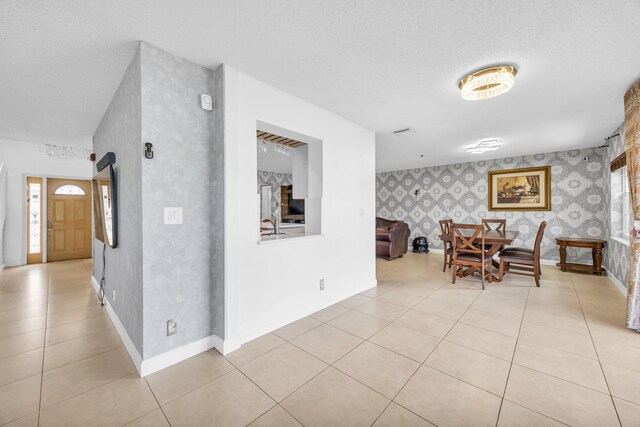 interior space featuring baseboards, a textured ceiling, wallpapered walls, and light tile patterned floors