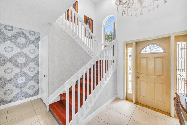 tiled entryway with a healthy amount of sunlight, baseboards, an inviting chandelier, and stairs
