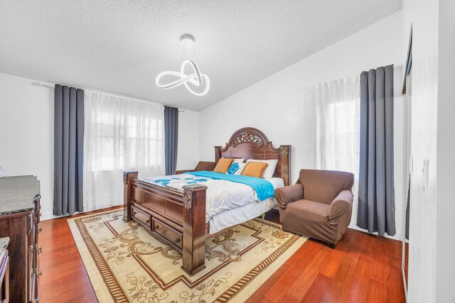 bedroom featuring a textured ceiling, an inviting chandelier, wood finished floors, and lofted ceiling