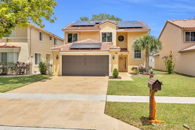 mediterranean / spanish-style house featuring a tiled roof, driveway, solar panels, a front yard, and stucco siding