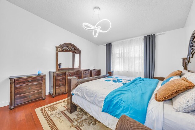 bedroom with a textured ceiling, a notable chandelier, wood finished floors, baseboards, and lofted ceiling