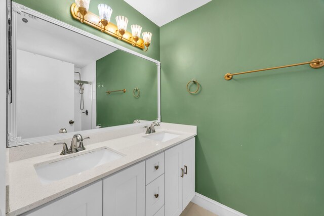 bathroom featuring double vanity, baseboards, a sink, and a shower