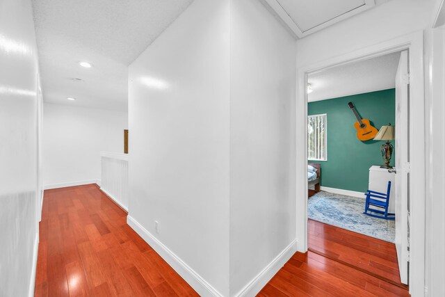 corridor featuring baseboards, recessed lighting, and wood finished floors