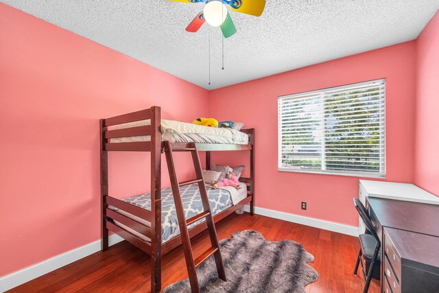 bedroom with a textured ceiling, baseboards, ceiling fan, and wood finished floors