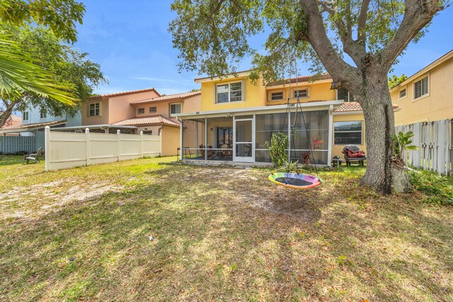rear view of property featuring a tile roof, stucco siding, a sunroom, a fenced backyard, and a yard