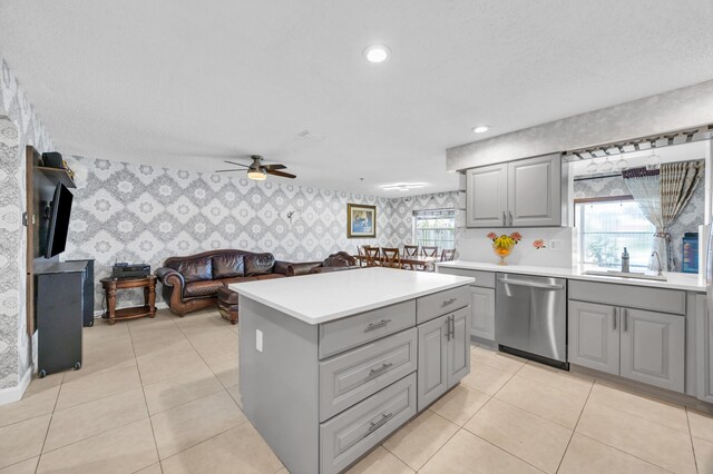 kitchen featuring stainless steel dishwasher, a sink, gray cabinetry, and wallpapered walls