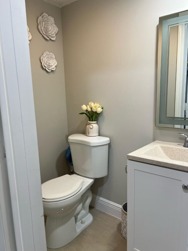 half bath with toilet, baseboards, tile patterned flooring, and vanity