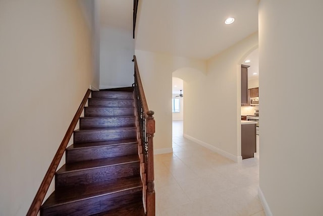 staircase with arched walkways, baseboards, tile patterned floors, and recessed lighting