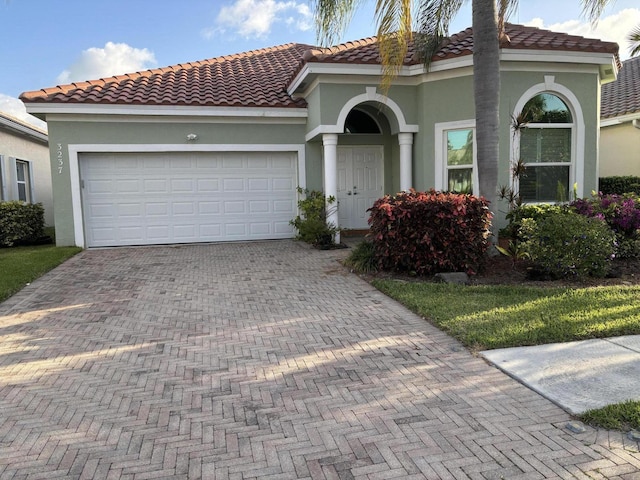 mediterranean / spanish-style house with a garage, decorative driveway, stucco siding, and a tiled roof