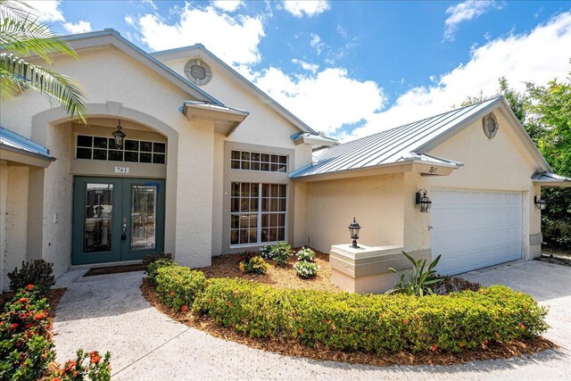 761 SW Lighthouse Dr, Palm City, FL 34990 - view of front of home with a garage, stucco siding, french doors, a standing seam roof, and driveway