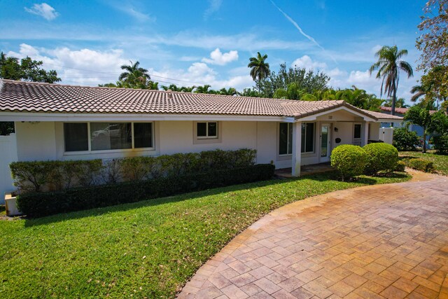 ranch-style house with a front lawn, stucco siding, and a tiled roof