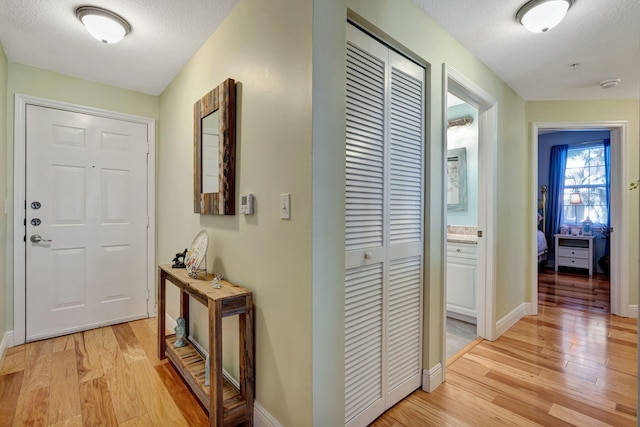 corridor with light wood-style floors, baseboards, and a textured ceiling