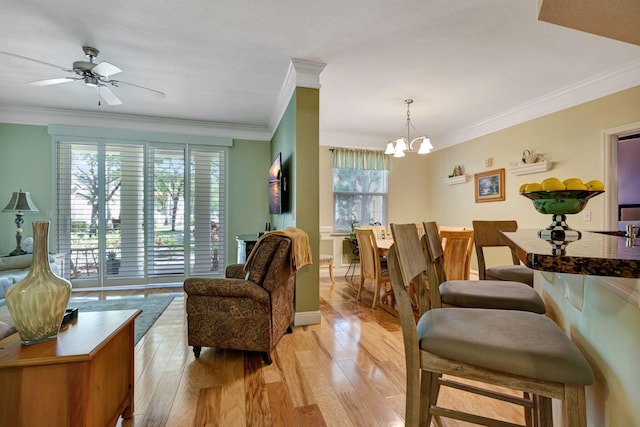 living area featuring crown molding, light wood-style floors, and ceiling fan with notable chandelier