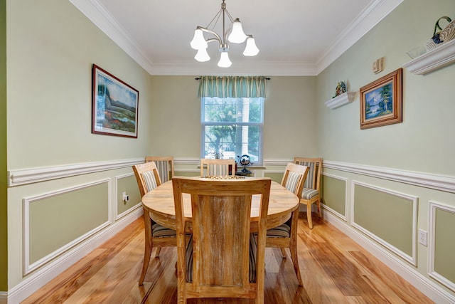 dining area featuring light wood-type flooring, crown molding, a decorative wall, and a chandelier