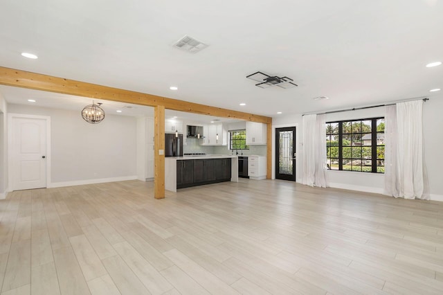 unfurnished living room with a notable chandelier, light wood-type flooring, visible vents, baseboards, and recessed lighting