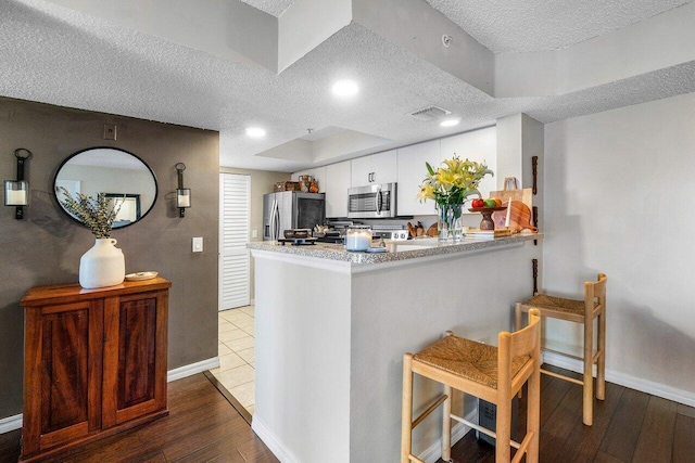 5031 Wiles Rd Unit 104, Coconut Creek, FL 33073 - kitchen with a textured ceiling, visible vents, appliances with stainless steel finishes, a peninsula, and white cabinetry
