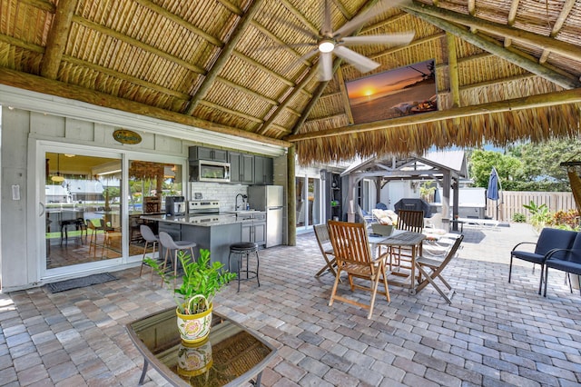 view of patio / terrace featuring ceiling fan, fence, an outdoor kitchen, a gazebo, and a bar