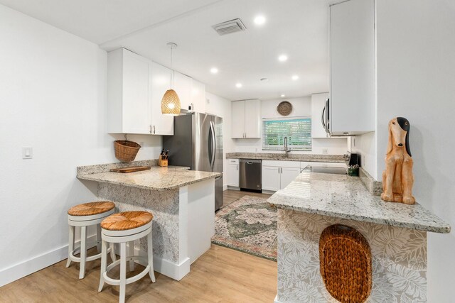 kitchen with light stone countertops, appliances with stainless steel finishes, a sink, a peninsula, and visible vents