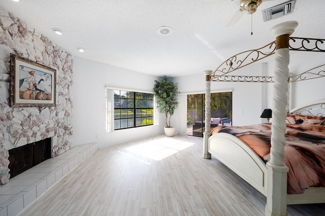 bedroom featuring access to outside, a textured ceiling, a tiled fireplace, wood finished floors, and visible vents