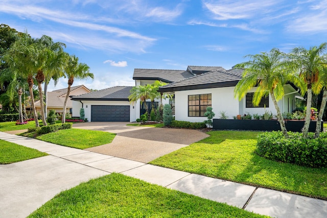 view of front of house featuring driveway, a tile roof, a front yard, an attached garage, and stucco siding