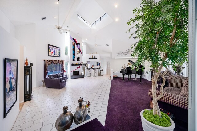 living area with ceiling fan, tile patterned flooring, high vaulted ceiling, a skylight, and visible vents