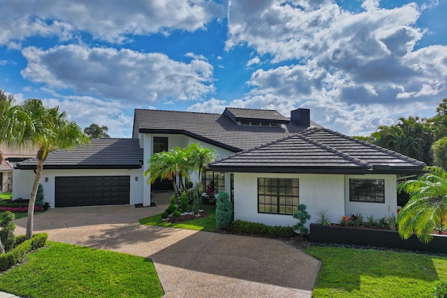 view of front of home featuring an attached garage, stucco siding, a front yard, concrete driveway, and a tiled roof