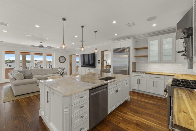 103 River Dr, Tequesta, FL 33469 - kitchen featuring appliances with stainless steel finishes, a sink, butcher block counters, wall chimney range hood, and white cabinets