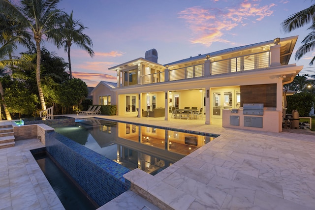 103 River Dr, Tequesta, FL 33469 - back of house at dusk featuring an outdoor kitchen, a balcony, an infinity pool, and a patio