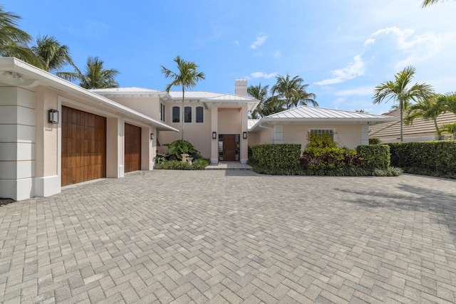 103 River Dr, Tequesta, FL 33469 - view of front of home with a garage, a standing seam roof, stucco siding, a chimney, and decorative driveway
