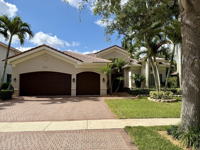 mediterranean / spanish-style home with a garage, a front yard, decorative driveway, stucco siding, and a tiled roof