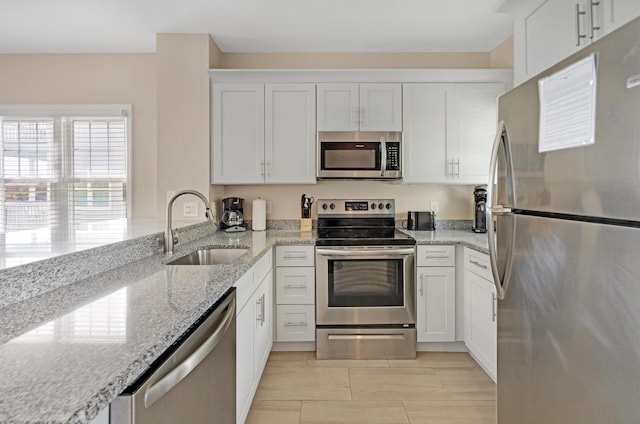 kitchen with a peninsula, white cabinetry, light stone counters, a sink, and stainless steel appliances