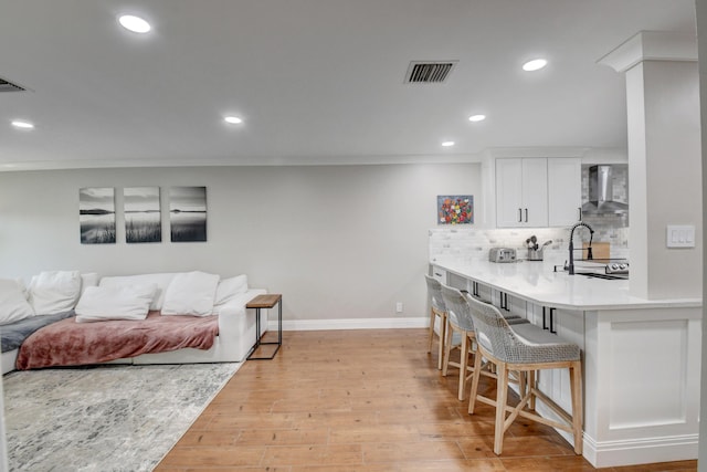 kitchen with visible vents, a breakfast bar area, recessed lighting, wall chimney exhaust hood, and light wood finished floors