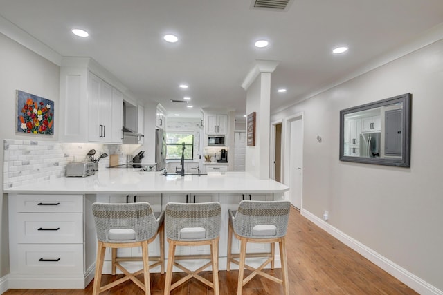 kitchen with backsplash, a sink, stainless steel fridge with ice dispenser, a peninsula, and a breakfast bar